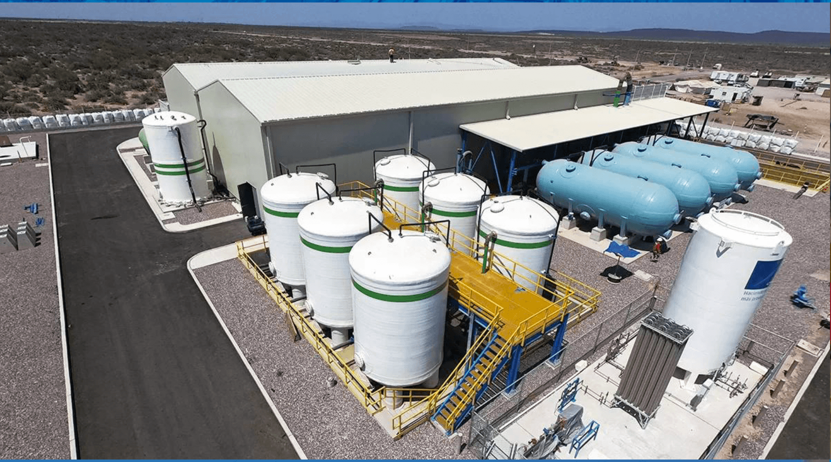 White vertical FRP tanks, a yellow railed platform and horizontal vessels at an industrial plant in a desert setting