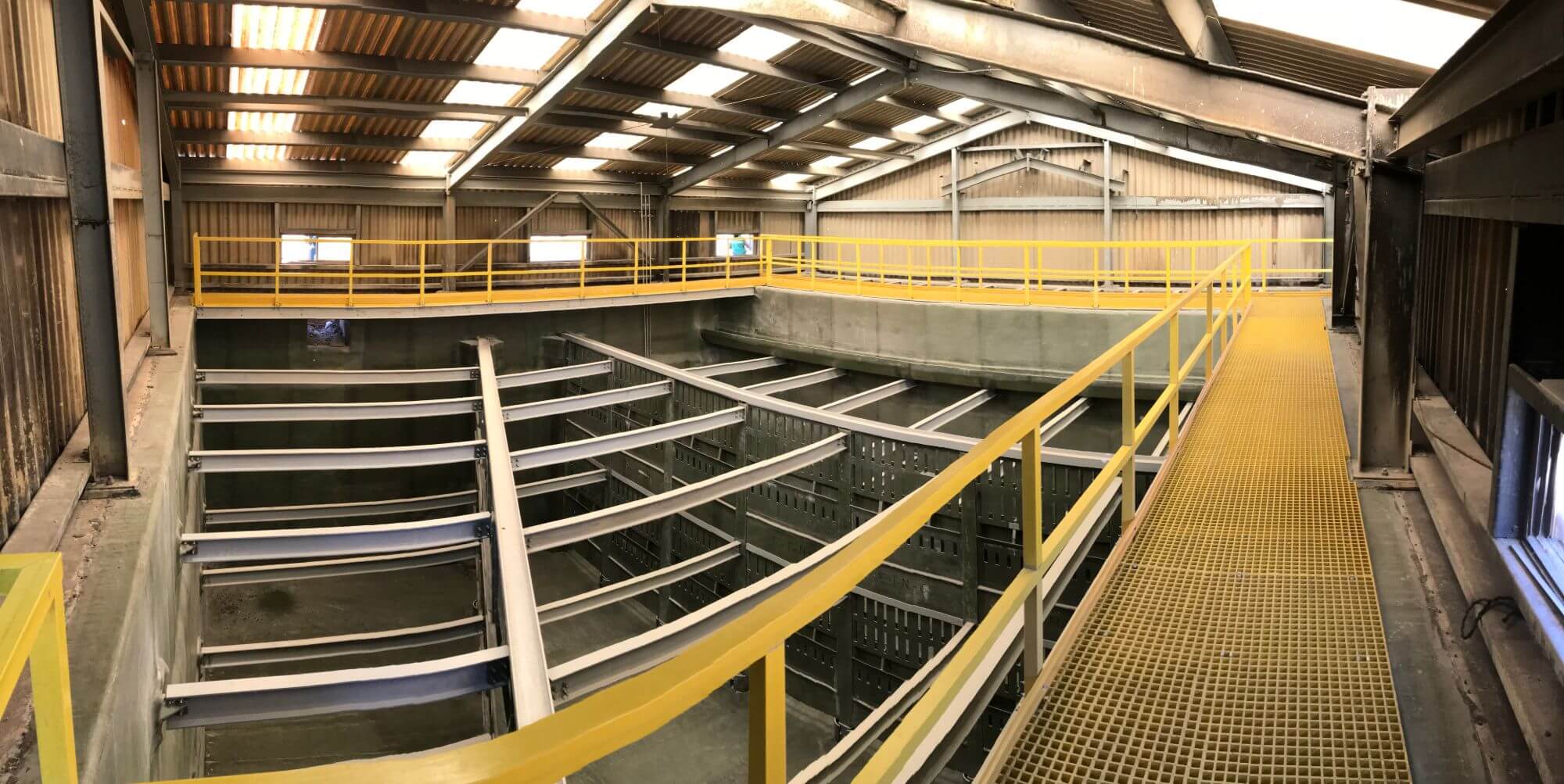 FRP grating walkway, yellow handrails, and pultruded beams inside a steel-framed process building
