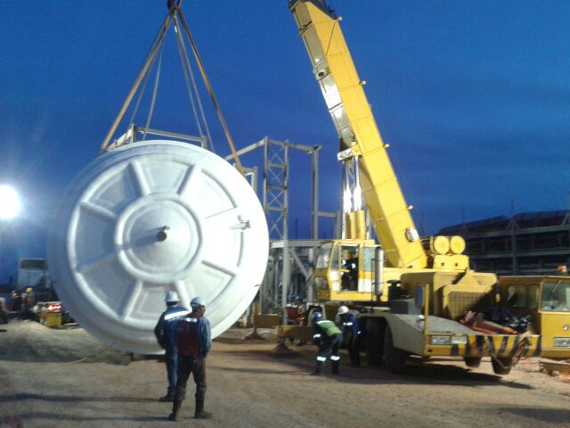 Large-diameter FRP tank lifted by crane during installation at a mining plant, with assembly crew