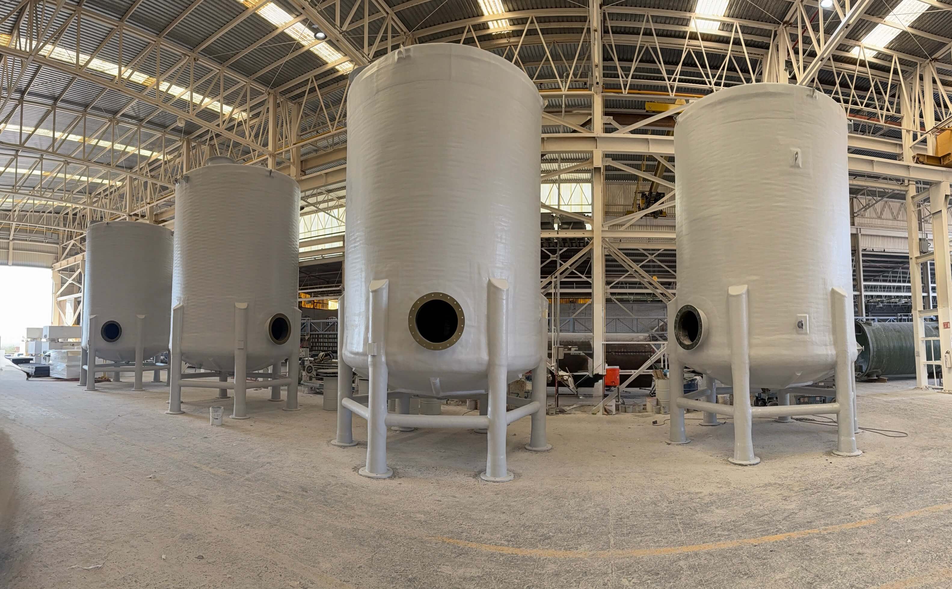 Fila de tanques de FRP blancos con fondo cónico y boquillas bridadas en la planta de fabricación de fibra de vidrio de Plastimarmol
