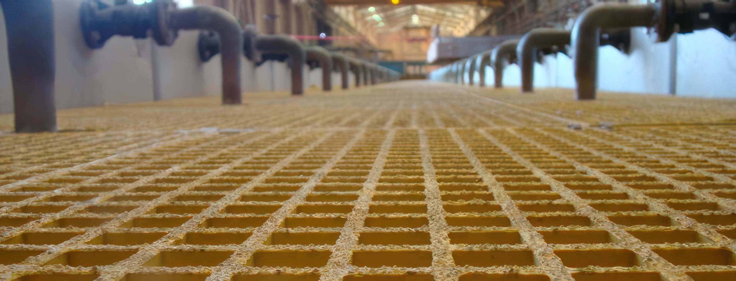 Yellow FRP molded grating walkway in an industrial plant with flanged piping runs on both sides