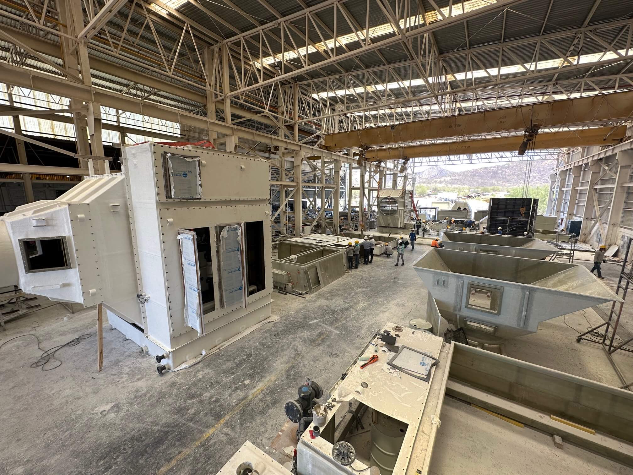 Ductos de scrubber y tolvas fabricadas en FRP, en piso de planta de Plastimarmol, con grúa viajera y trabajadores al fondo
